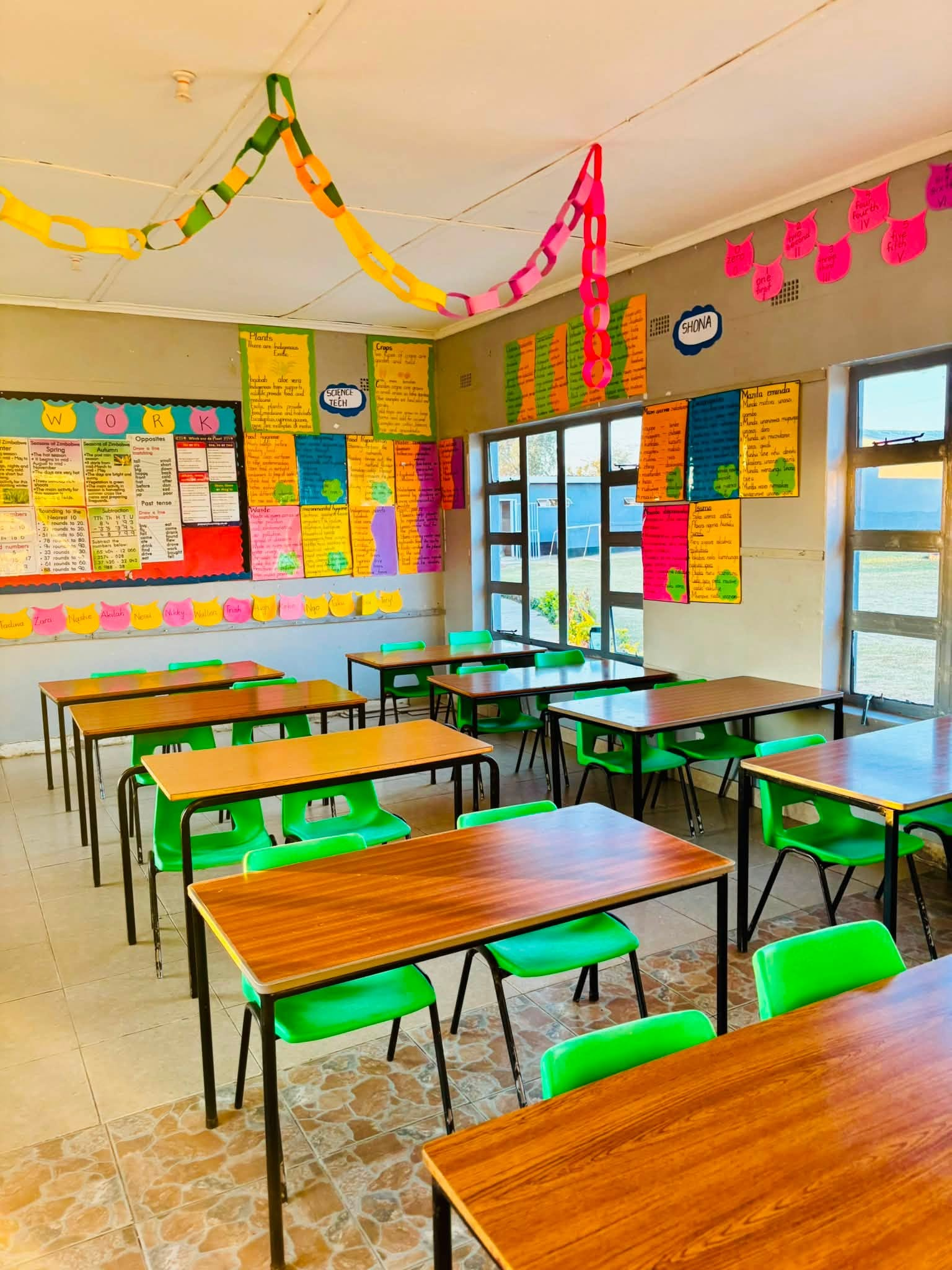 A bright classroom with green chairs and pupil work on the walls